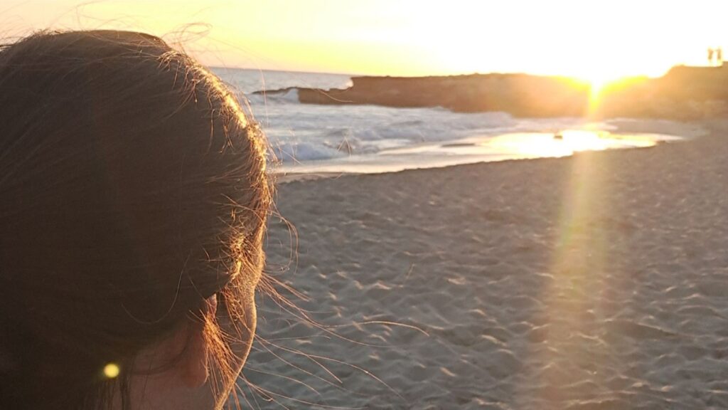 mujer mirando una puesta de sol en la playa, momento de calma y relax